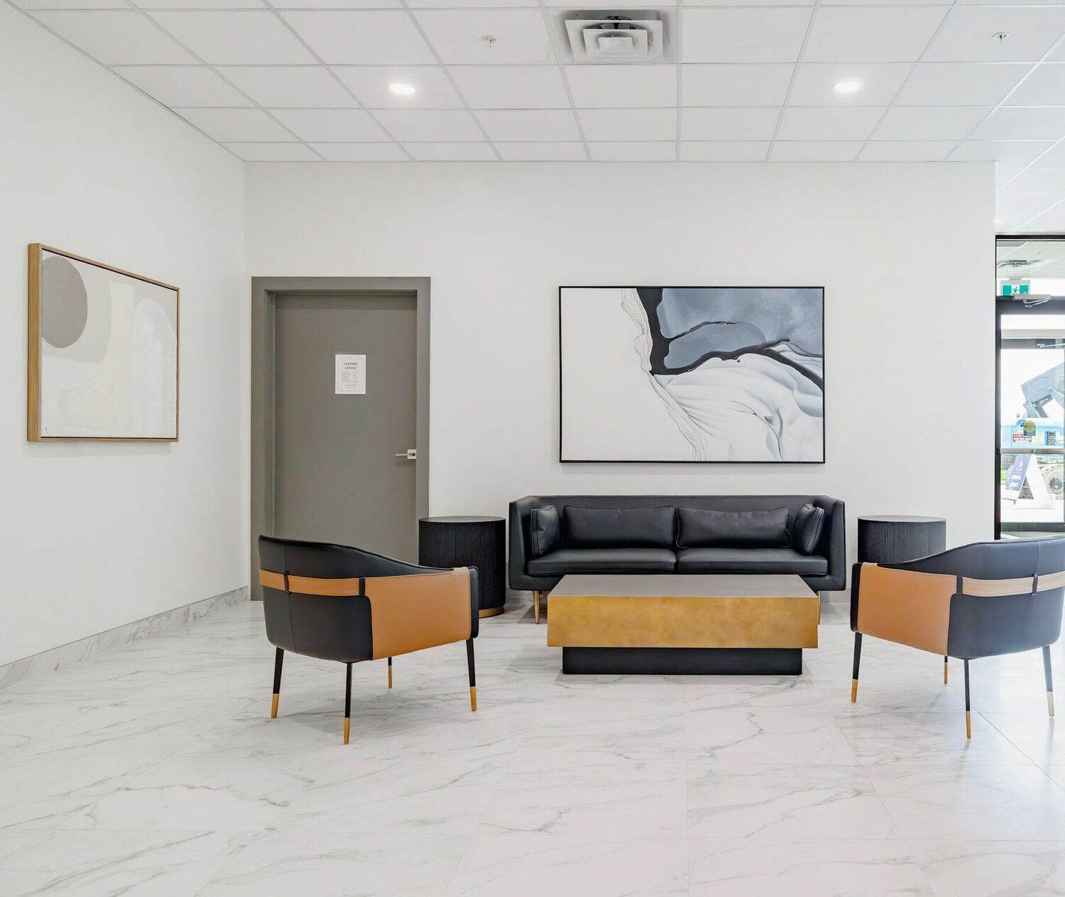 A bright waiting room with a black sofa, two chairs and a table